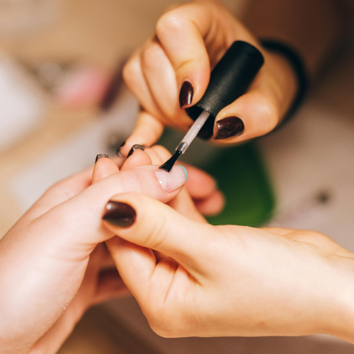 A pair of hands applies nail polish to a different hand.